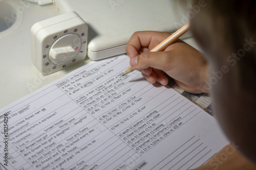 Home education. Home work after school. Boy  with pen writing english test by hand on traditional white notepad paper.  photo