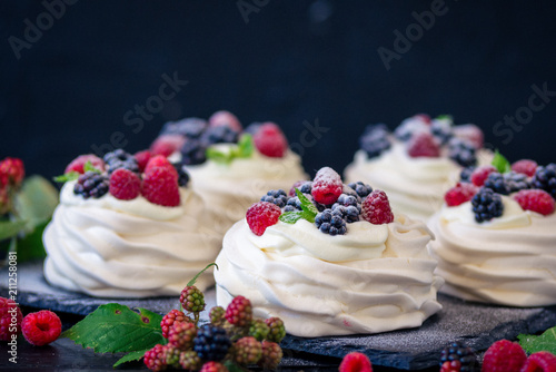 Photos Homemade meringue basis for cake Pavlova with fresh blueberries and BlackBerry and powdered sugar on black concrete texture background