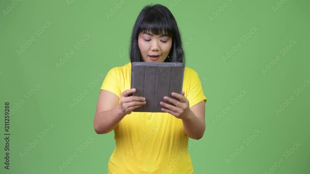 Beautiful happy Asian woman using digital tablet and looking surprised Beautiful happy Asian woman using digital tablet and looking surprised