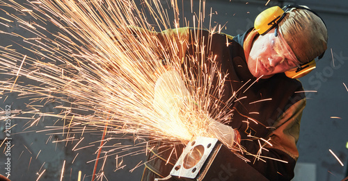 Fotografija worker grinding weld seam with grinder machine and sparks