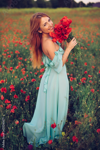 happy red-haired woman walking with bouquet in hands on flowering poppy field