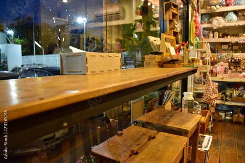 A counter bar made from wood is in the coffee cafe in the evening. There are mini decor on the counter and shelf.