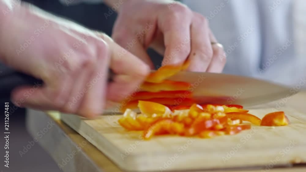 Close up hands of unrecognizable cook using knife when chopping red bell peppers on cutting board Close up hands of unrecognizable cook using knife when chopping red bell peppers on cutting board