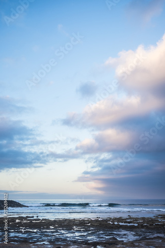 scenic landscape in early morning sunrsie for ocean rocks beach and waves for young surfers on the background. blue beautiful sky with sweet clouds. blue hours and magic colours