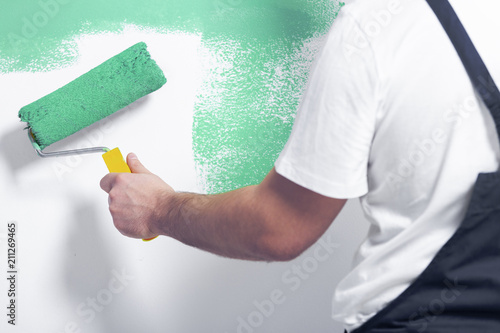 Close-up of worker with roller painting white wall on green photo