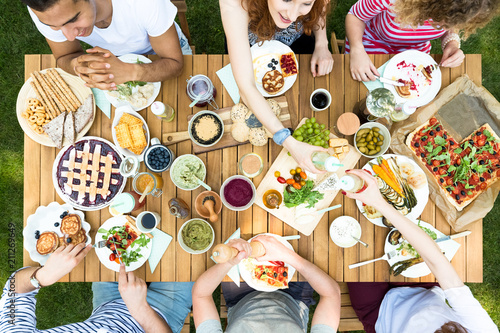 Top view on garden table with pastry, fruits and pizza during meeting of friends