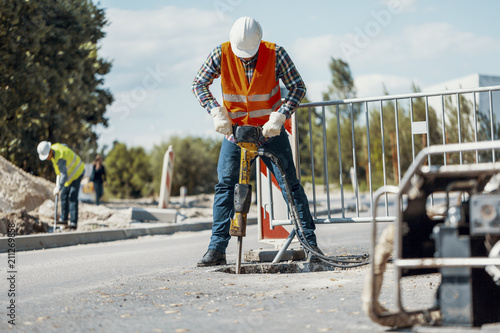 Worker in reflective vest with drill repairing street during roadworks photo