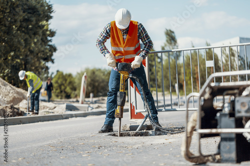 Foto Worker in reflective vest with drill repairing street during roadworks