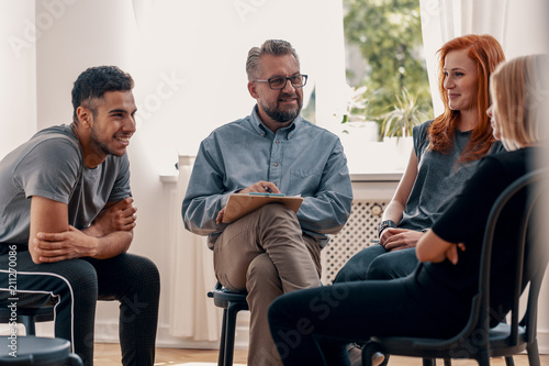 Fototapeta Naklejka Na Ścianę i Meble -  Smiling spanish man talking with friends during meeting for teenagers with therapist