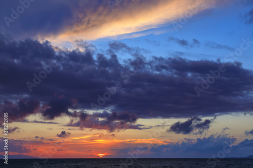 Amazing striped yellow and red sky with cloud formations over endless ocean.