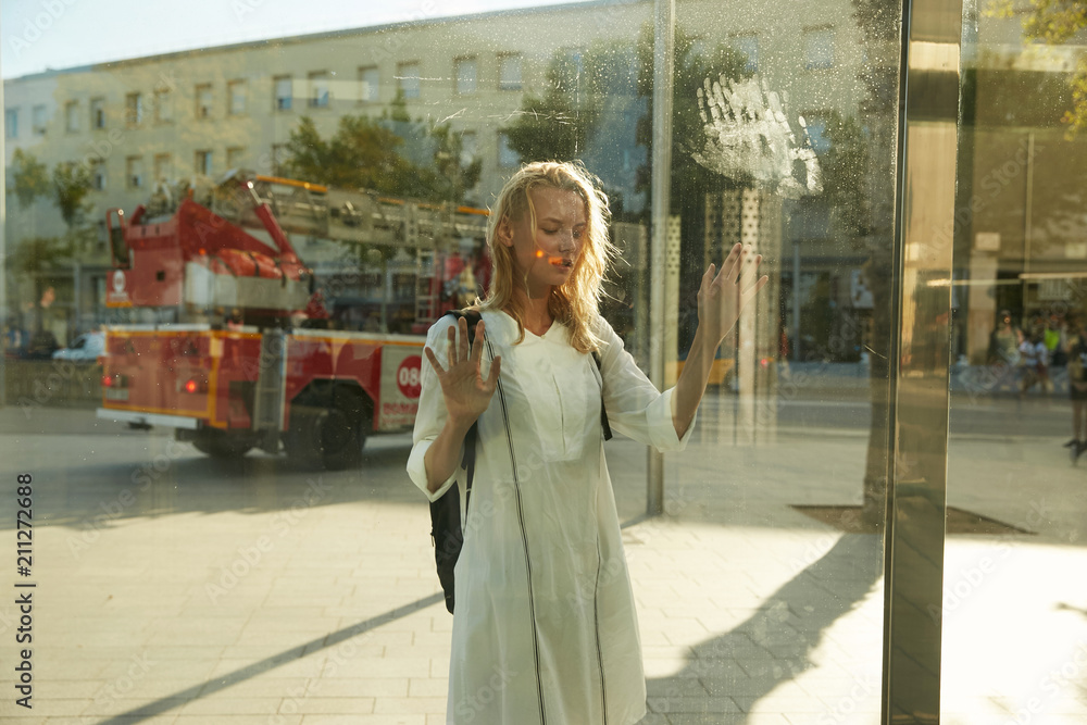 A blonde model girl standing at a bus stop, view through glass, with fire truck with alarming feeling A blonde model girl standing at a bus stop, view through glass, with fire truck with alarming feeling