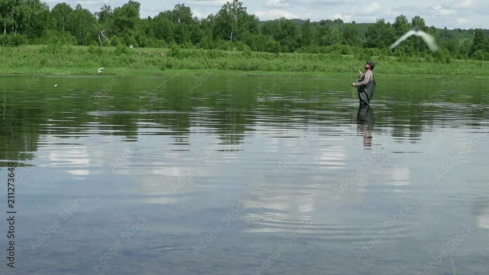 Joyful fisherman is fishing in calm river water near the shore Joyful fisherman is fishing in calm river water near the shore