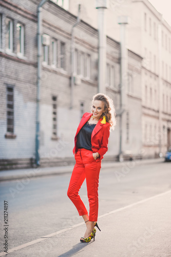 Portrait of a beautiful bright girl street style lifestyle smiling and posing in a red suit on a sunny day