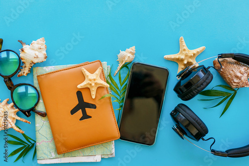 planning summer vacation concept. travel and wanderlust flat lay. passport, map, phone, sunglasses, headphones on blue trendy paper with shells. stylish creative image