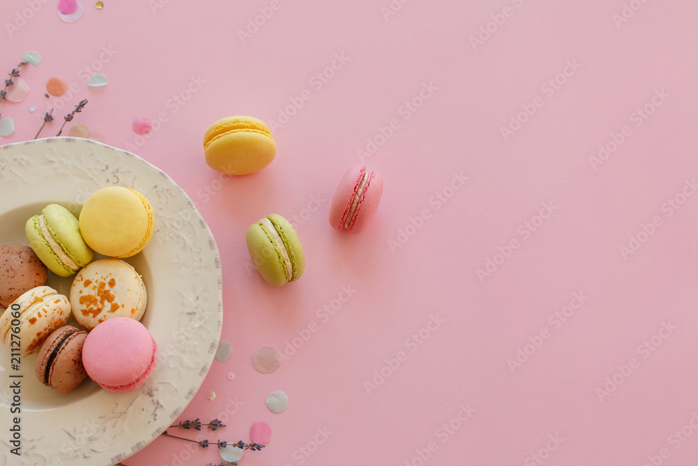 food photography flat lay of tasty colorful macarons in vintage plate on trendy pastel pink paper with lavender and confetti. space for text pink, yellow, green, white, brown macaroons. food photography flat lay of tasty colorful macarons in vintage plate on trendy pastel pink paper with lavender and confetti. space for text pink, yellow, green, white, brown macaroons.