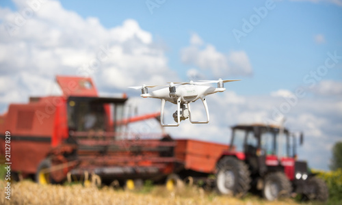 Drone in front of tractor and combine harvester in field