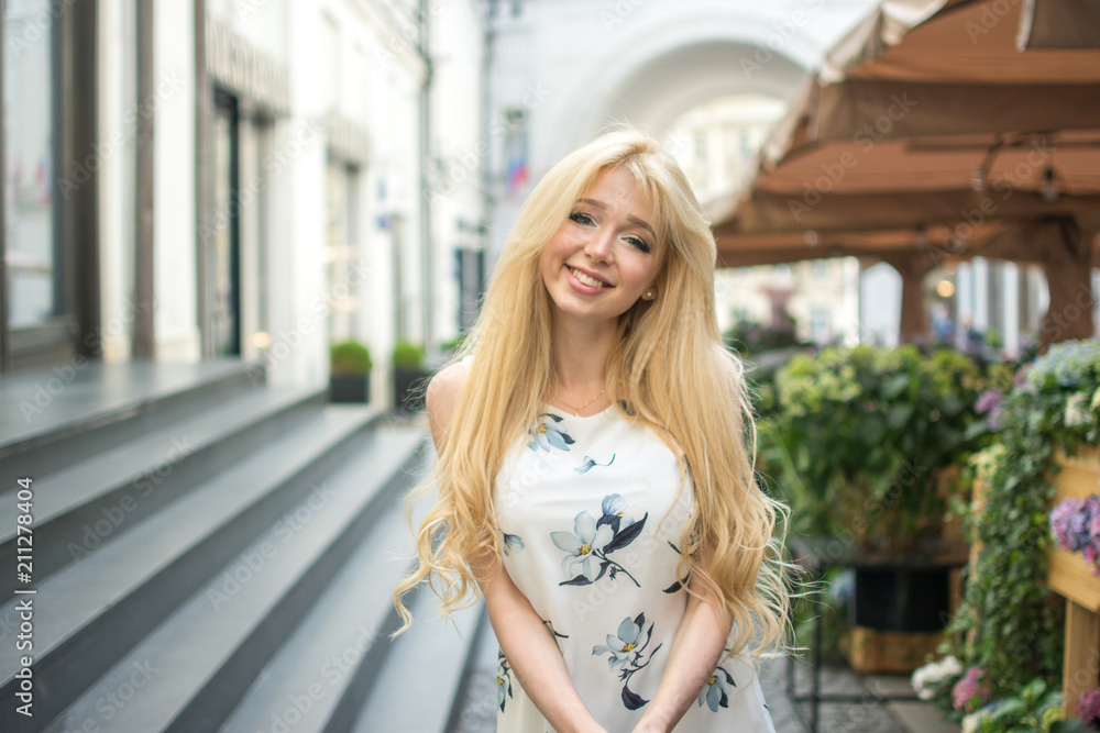 Beautiful young woman with perfect blonde hair wearing dress looking at camera and posing in the city street. Beautiful young woman with perfect blonde hair wearing dress looking at camera and posing in the city street.