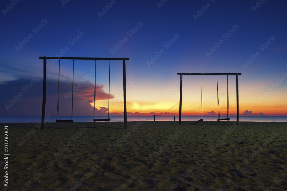 silhouette set of swing on the sandy beach over stunning sunrise background