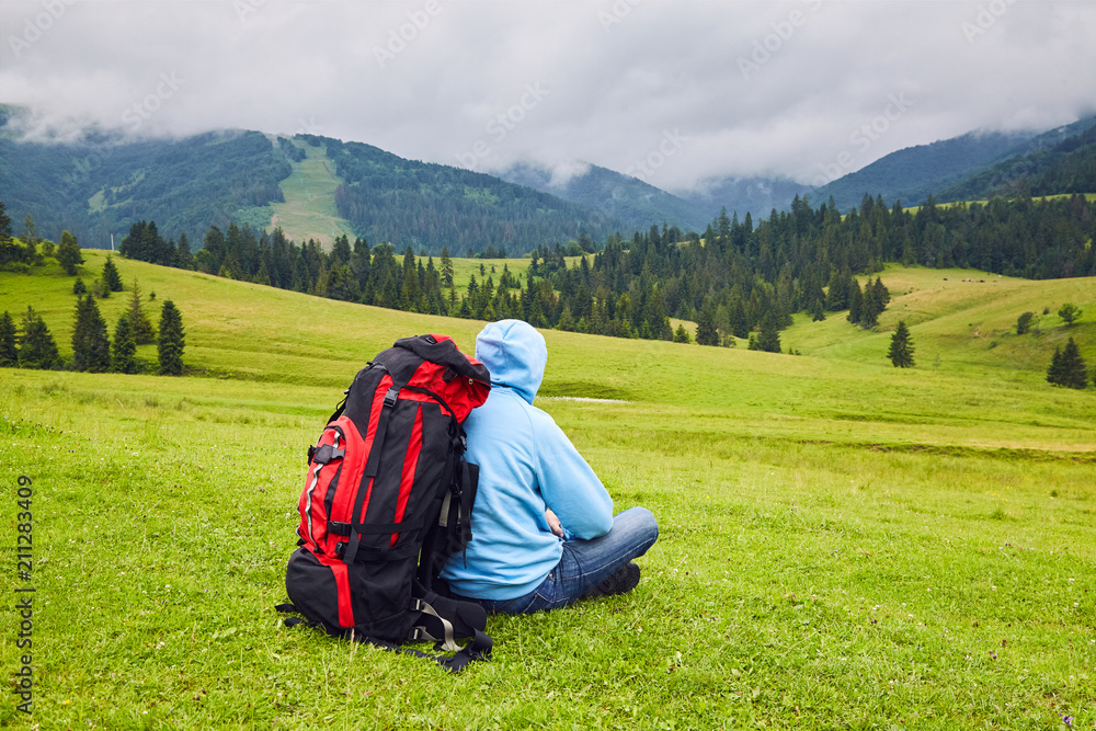 Hill walker is sitting in the middle of mountain wilderness. Traveler man in the field. Man with backpack hiking in mountains Travel Lifestyle success concept adventure active vacations outdoor Hill walker is sitting in the middle of mountain wilderness. Traveler man in the field. Man with backpack hiking in mountains Travel Lifestyle success concept adventure active vacations outdoor