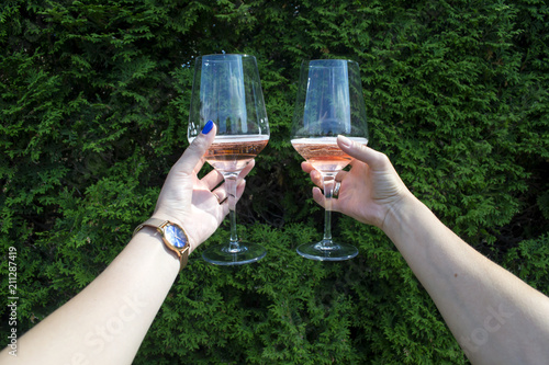 A glass of wine in women's hands against a natural background. Two friends cheering. Drinking wine.