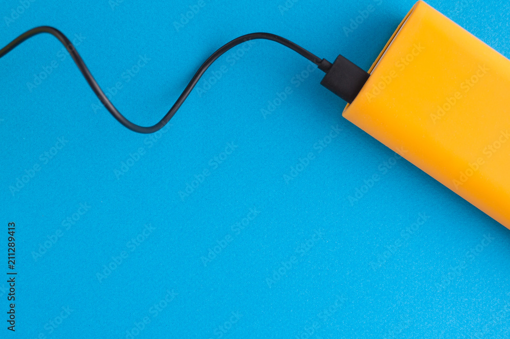 Orange power bank plugged in with black USB cable on an blue background Orange power bank plugged in with black USB cable on an blue background