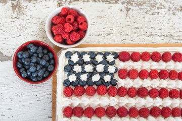 Patriotic, red white and blue, American flag cake, decorated with fresh blueberries and raspberries. Top view against white wooden table. Concept for Fourth of July celebration.