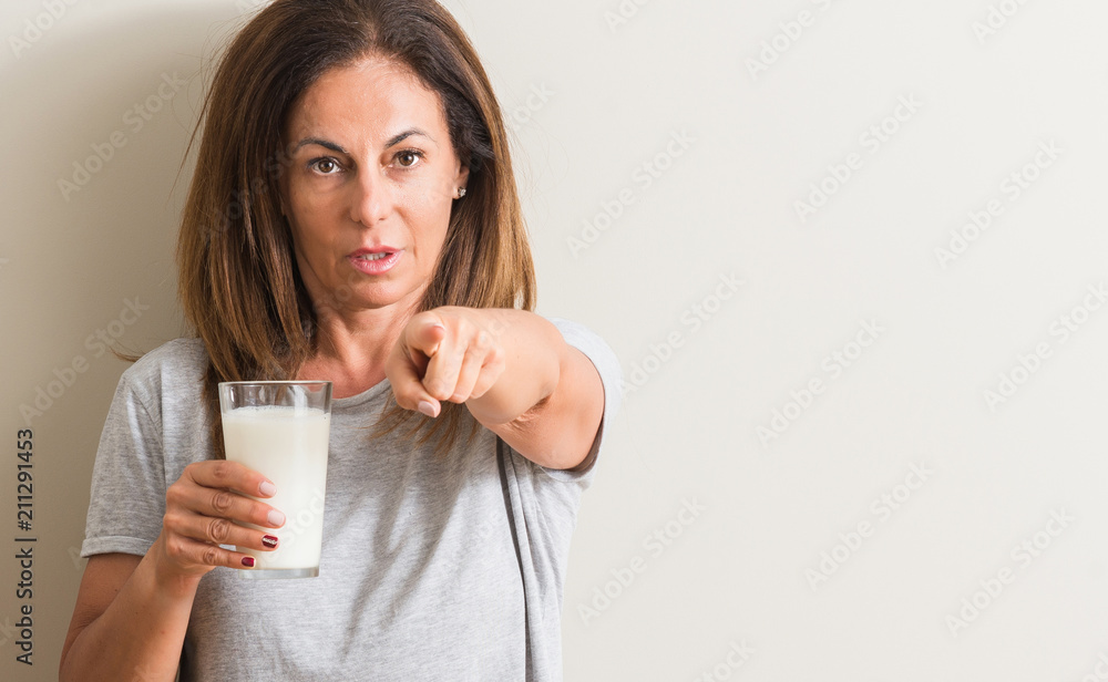Middle age woman drinking a glass of fresh milk pointing with finger to the camera and to you, hand sign, positive and confident gesture from the front Middle age woman drinking a glass of fresh milk pointing with finger to the camera and to you, hand sign, positive and confident gesture from the front