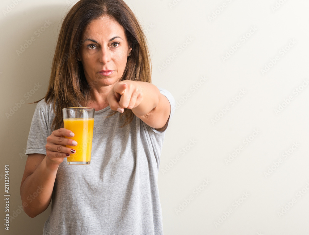Middle age woman drinking orange juice in a glass pointing with finger to the camera and to you, hand sign, positive and confident gesture from the front Middle age woman drinking orange juice in a glass pointing with finger to the camera and to you, hand sign, positive and confident gesture from the front