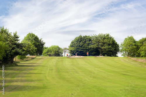 Golf field and three unrecognisable golf players at a distance