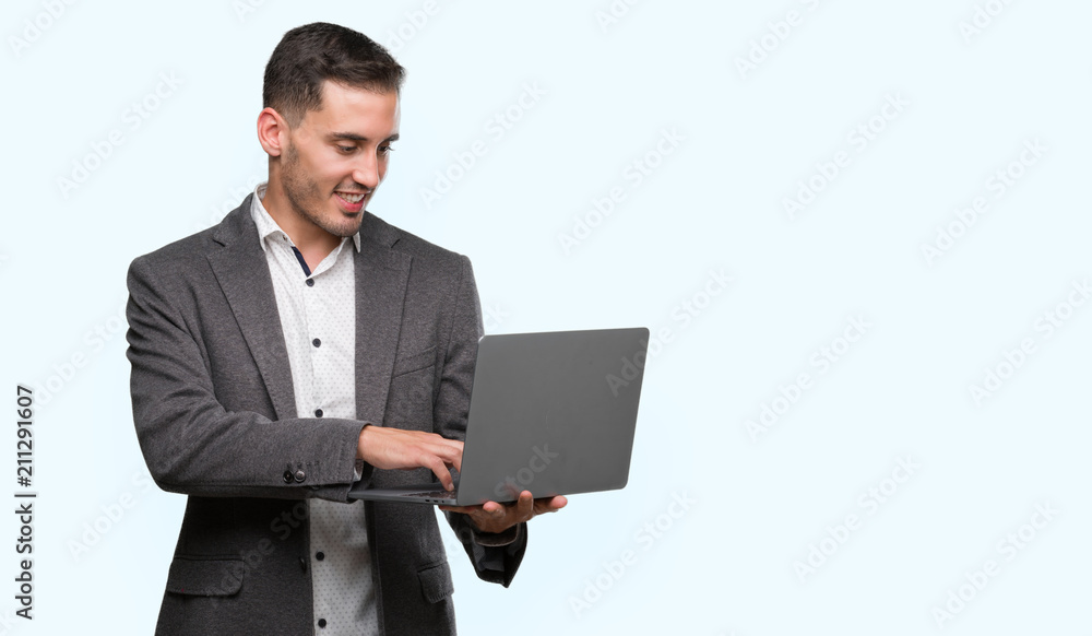 Handsome young man using computer laptop with a happy face standing and smiling with a confident smile showing teeth Handsome young man using computer laptop with a happy face standing and smiling with a confident smile showing teeth