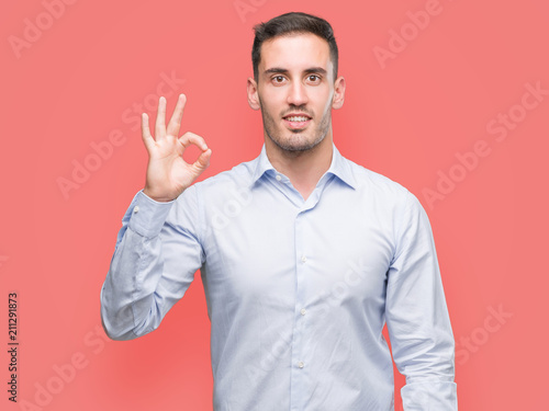 Handsome young businessman smiling positive doing ok sign with hand and fingers. Successful expression. © Krakenimages.com