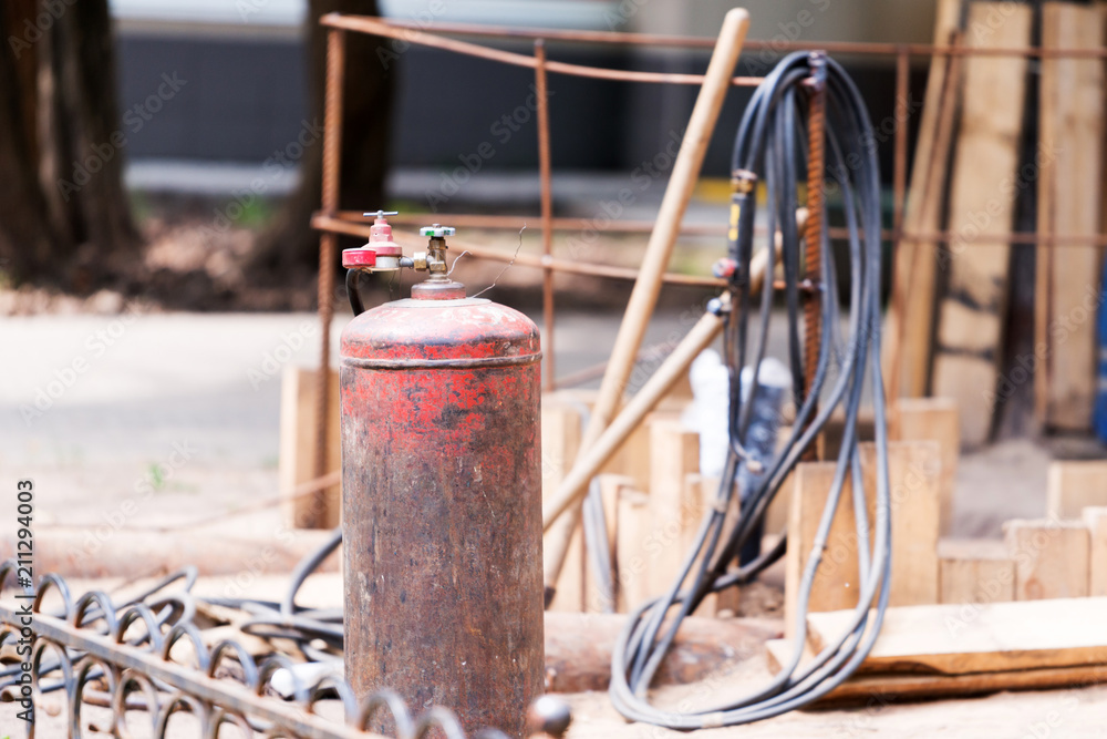 Old red propane tank on the background of hoses and construction