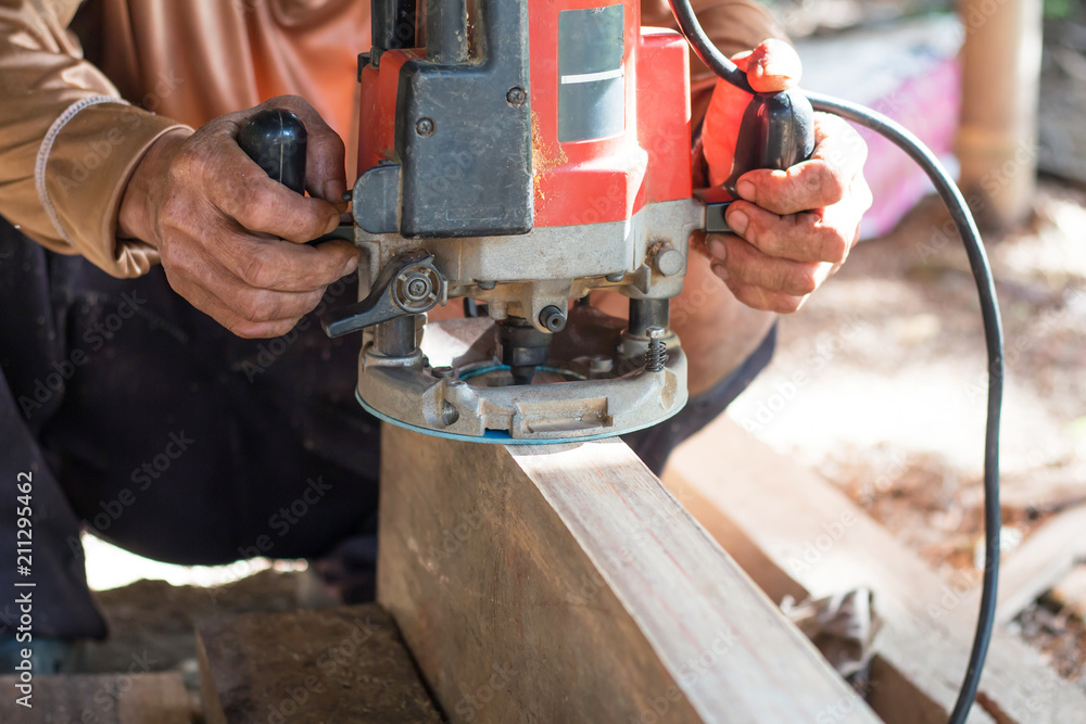 Hand of carpenter using electric planer with wooden plank in carpentry workshop Hand of carpenter using electric planer with wooden plank in carpentry workshop