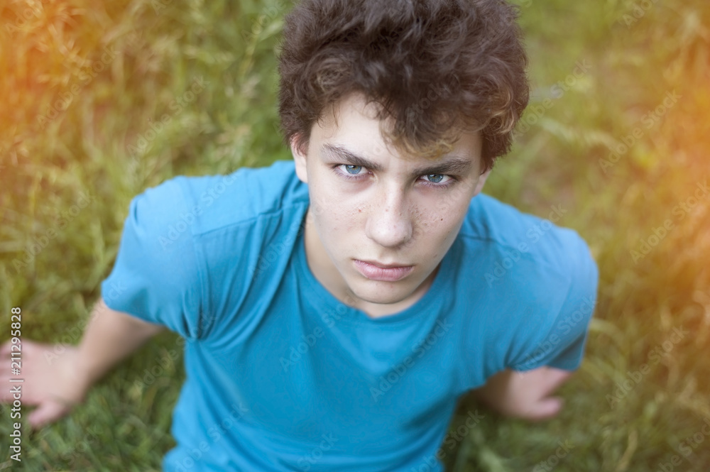 A sad teenager sits on the grass and looks upstairs. He suffers from pimples and acne on his face A sad teenager sits on the grass and looks upstairs. He suffers from pimples and acne on his face