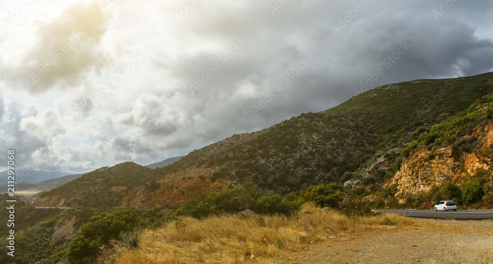 Asphalt road and cars in the mountains with cloudy sky on the background. Crete, Greece