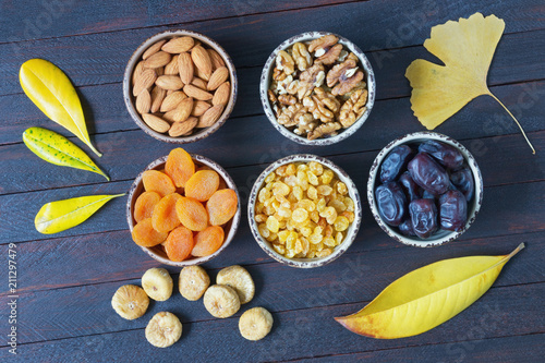 Autumn. Various nuts and dried fruits (walnuts, almonds,  dried apricots, raisins, date fruits, figs ) and yellow leaves on dark wooden table. Flat lay