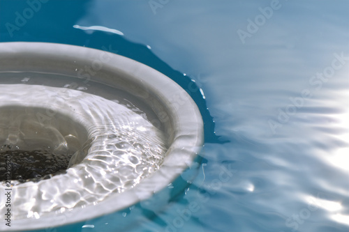 View of the surface of a swimming pool and to a skimmer into which the blue water flows in waves.
