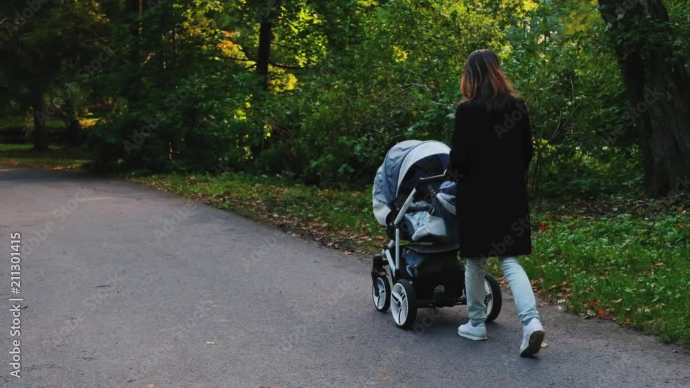 Mother walking with a pram in the park Mother walking with a pram in the park