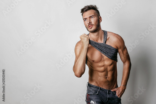 Fotografie Muscular model sports young man in blue jeans raised his hand t-shirt and showing his press on a grey background
