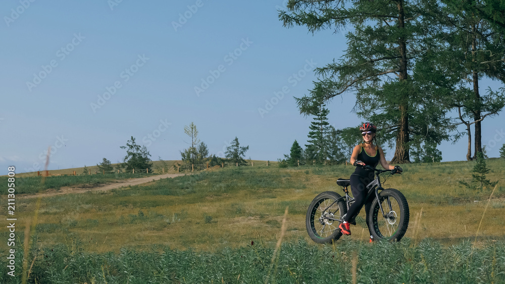 Fototapeta premium Fat bike also called fatbike or fat-tire bike in summer riding in the forest. Beautiful girl and her bicycle in the forest. She rolls her bike and poses to the operator.