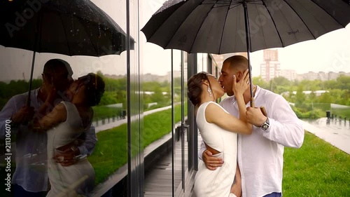 young couple in wedding clothes standing in the rain with an umbrella and kiss photo