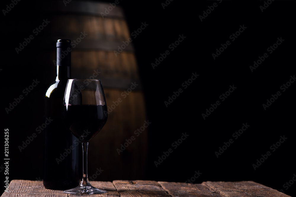 A bottle opf red wine and a glass with barrel on background