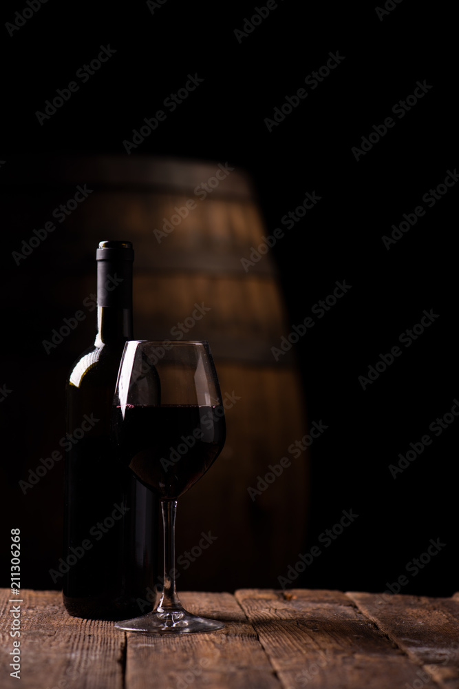 A bottle opf red wine and a glass with barrel on background