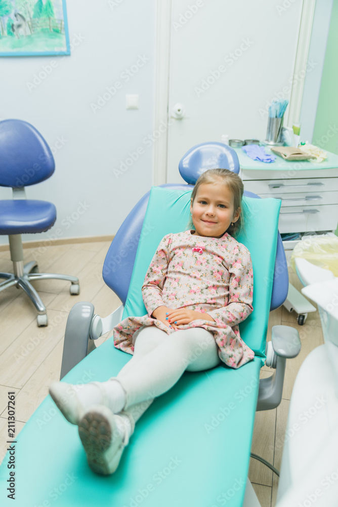 Child with a mother at a dentist's reception. The girl lies in the chair, behind her mother. The doctor works with an assistant. Procedure for drilling a tooth. Setting a temporary seal. Using the x Child with a mother at a dentist's reception. The girl lies in the chair, behind her mother. The doctor works with an assistant. Procedure for drilling a tooth. Setting a temporary seal. Using the x