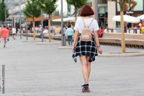 she rides on a skateboard down the street on a summer day