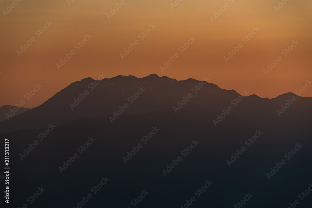 Sunset high in the mountains. Peaks of high mountains and golden clouds in the sky. Evening landscape.