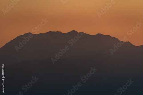 Sunset high in the mountains. Peaks of high mountains and golden clouds in the sky. Evening landscape.