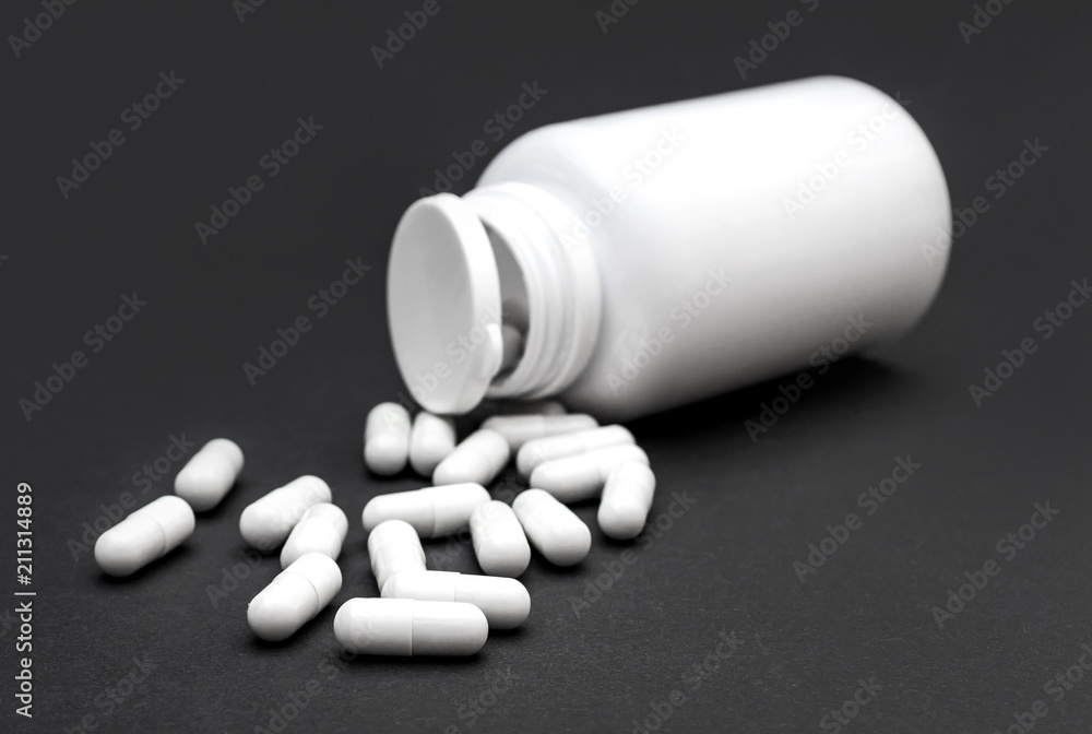 White pills with plastic bottle on black background.