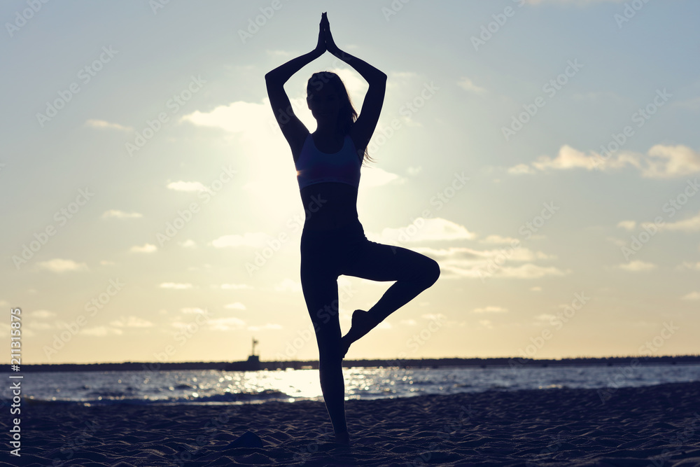 Silhouette young woman practicing yoga on the beach at sunset