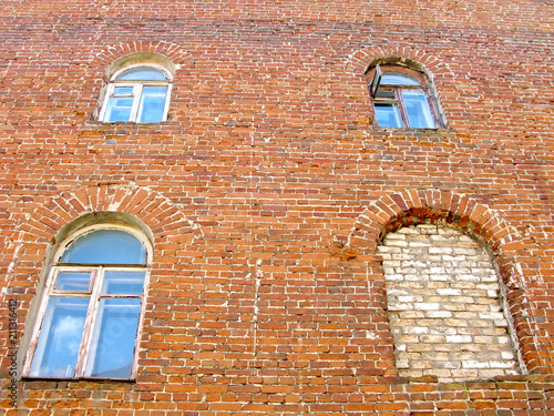 Brick wall of facade of old residential house. Windows have an arched shape. One of the four windows is sealed. On one of the upper floors is open the window leaf.